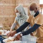 A woman and man are side by side preparing boxed meals as volunteers.