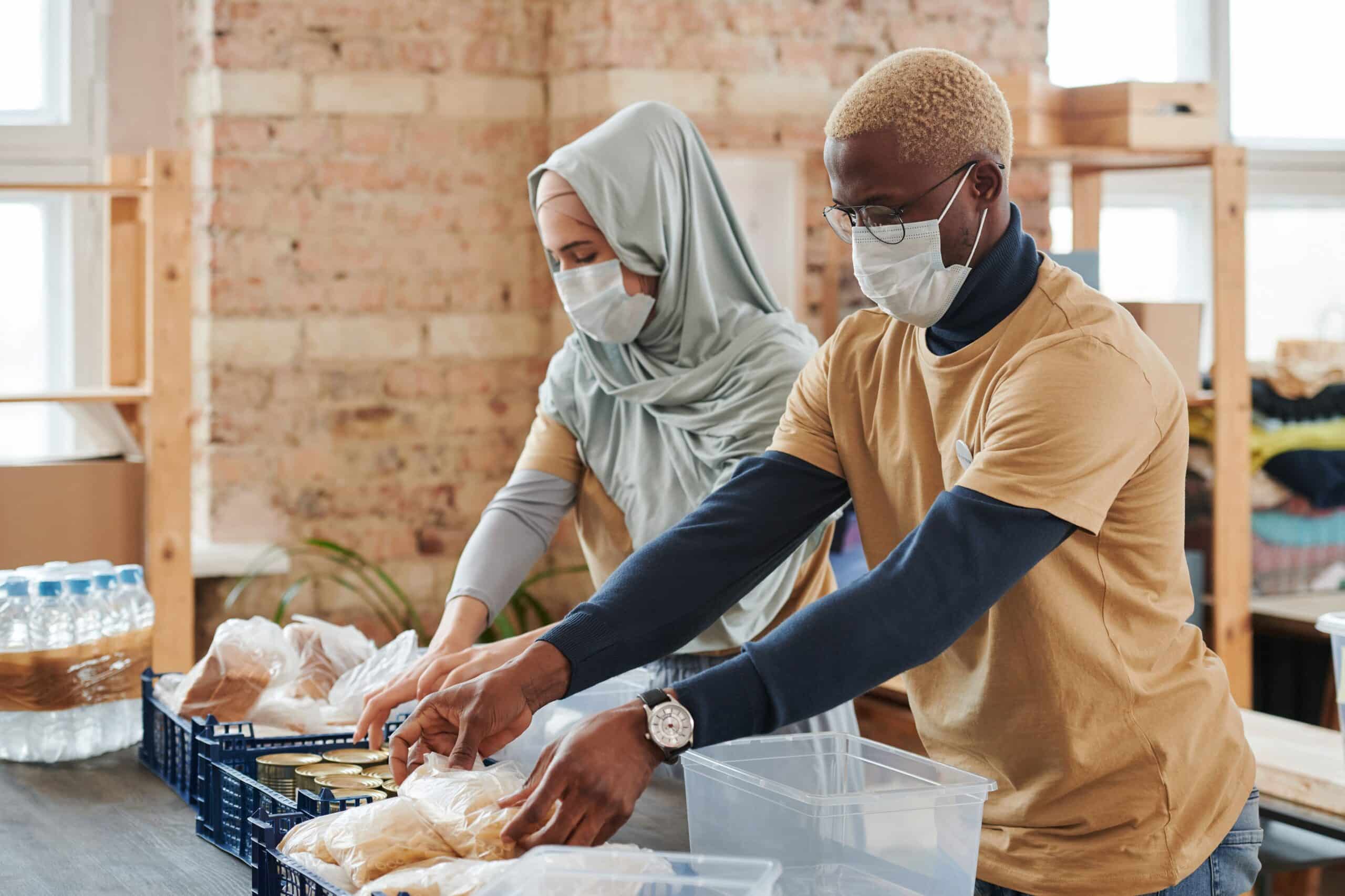 A woman and man are side by side preparing boxed meals as volunteers.
